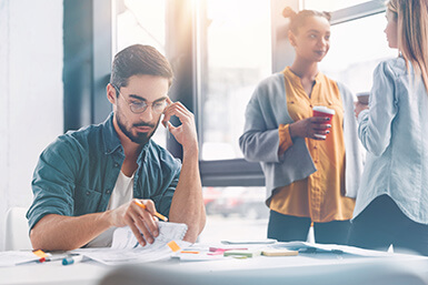 Young business man looking at reports with employees in background.