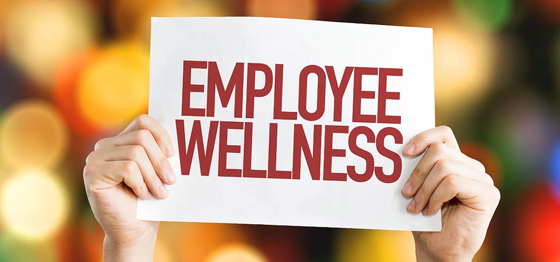 Employee holding an Employee Wellness sign.  Promoting employee wellness programs in our Boise, Garden City, Meridian, Idaho Falls, Pocatello and Rexburg locations.